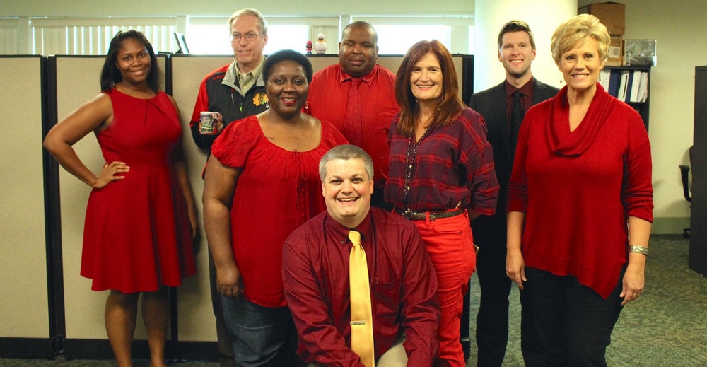 Wear Red Day: Eight men and women wearing red standing next to a wall and smiling.